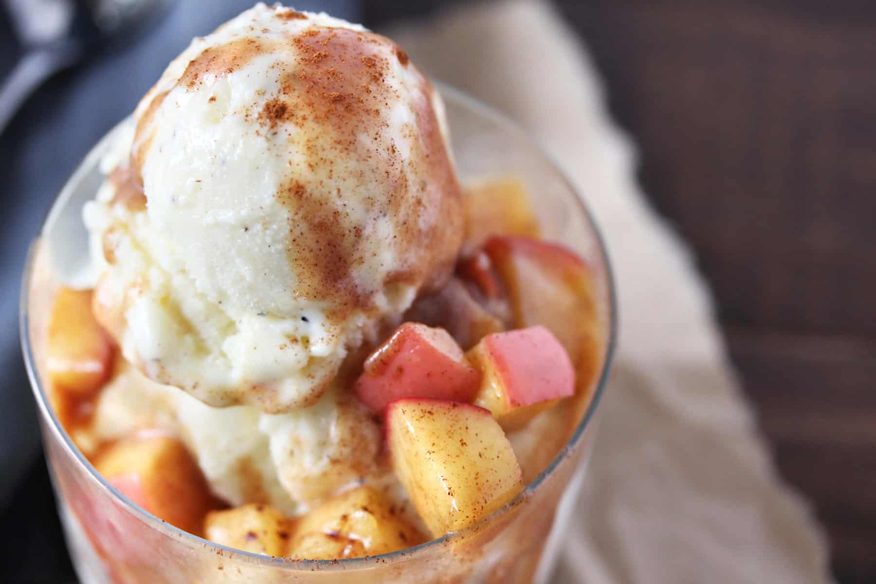 Vanilla ice cream with cinnamon apple topping in a clear glass on grey napkin.