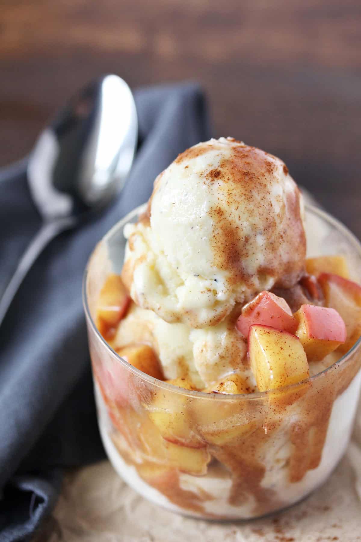 Vanilla ice cream with cinnamon apple topping in a clear glass on grey napkin.