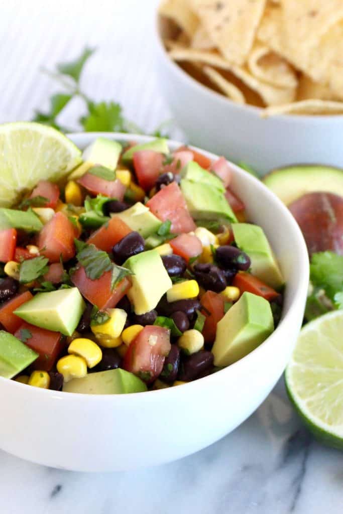 Black beans, corn, tomato and avocado in white bowl.