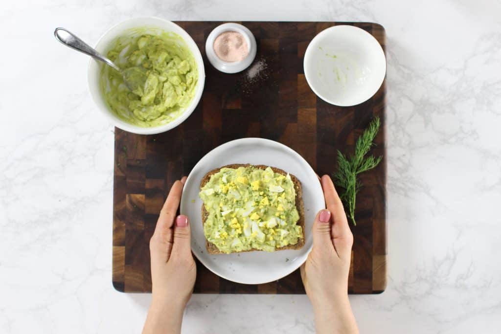 Avocado egg salad toast on white plate.