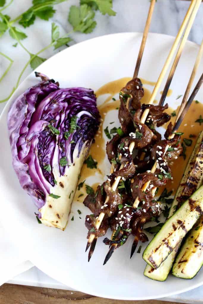 Beef skewers, grilled vegetables and peanut sauce on white plate.