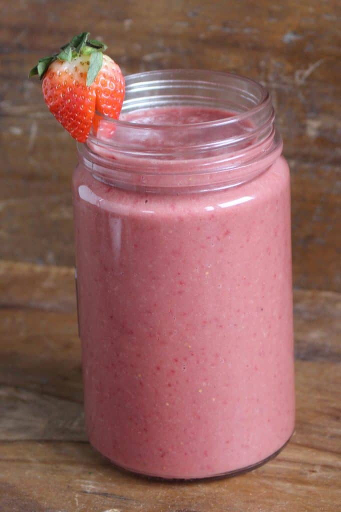 Pink smoothie in mason jar on wood surface.