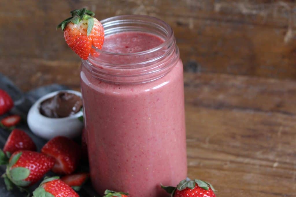 Pink smoothie in mason jar on wood surface.