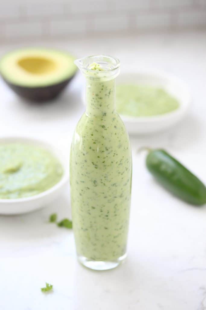 Green sauce in glass bottle on white surface.