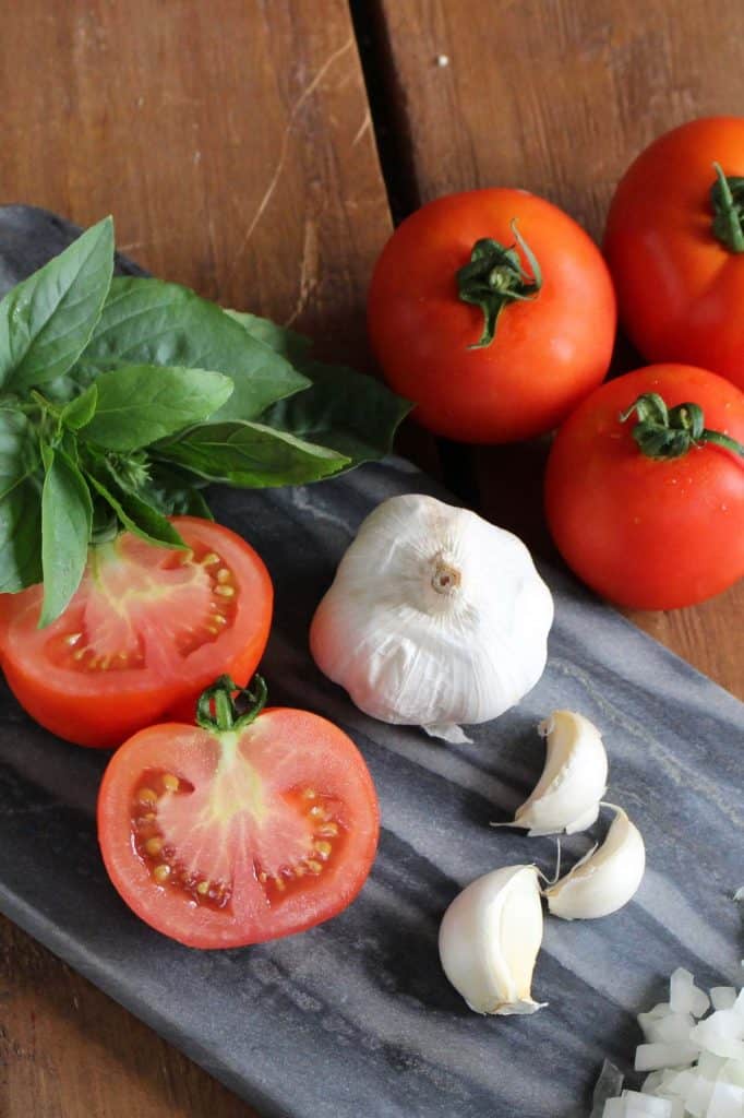 Tomatoes, basil, garlic and onion on blue cutting board.