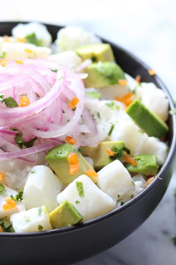 Fish, avocado and red onion in black bowl.