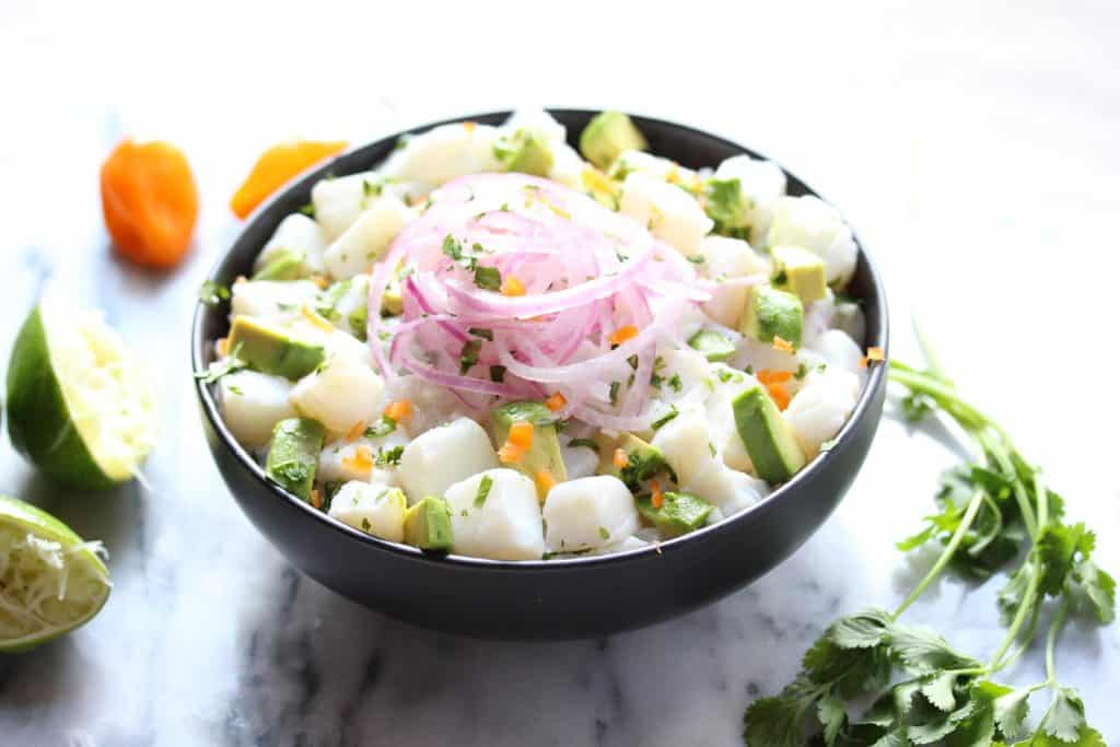 Fish, avocado and red onion in black bowl.