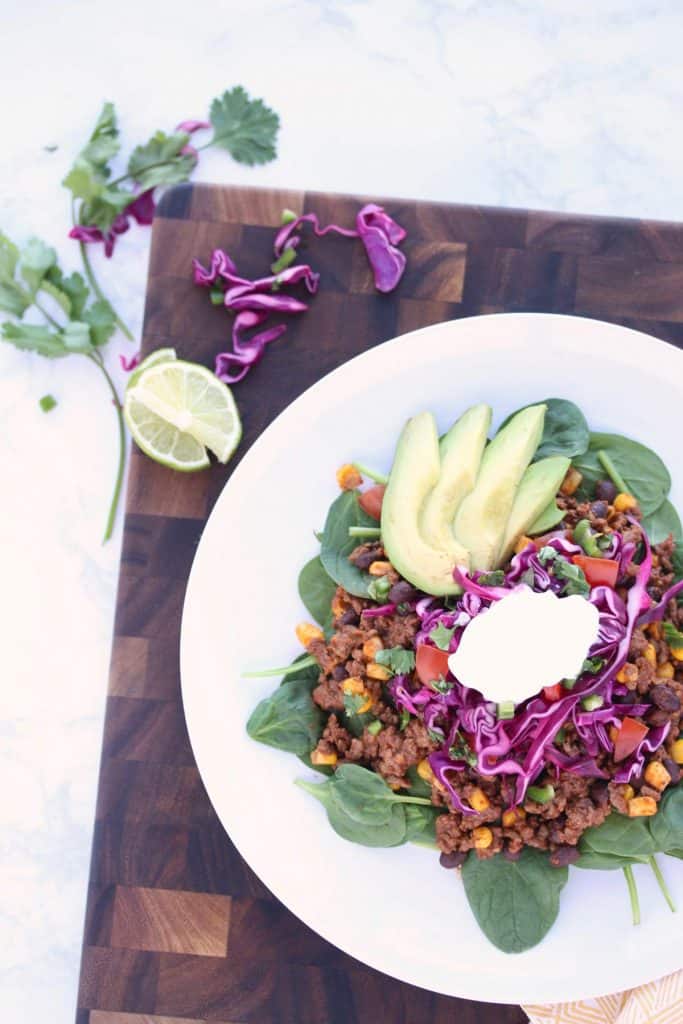 Taco salad on white plate on brown cutting board.