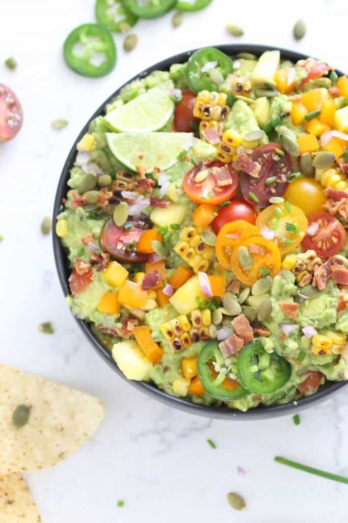 Guacamole in black bowl with corn, tomatoes, jalapeños and bacon