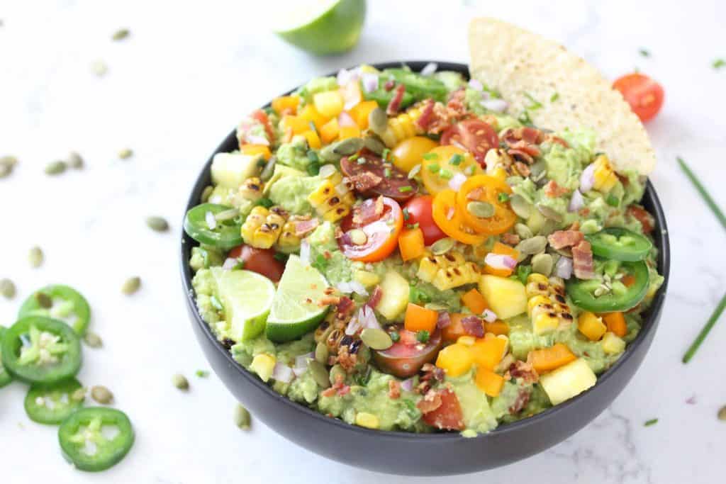 Guacamole in black bowl with corn, tomatoes, jalapeños and bacon