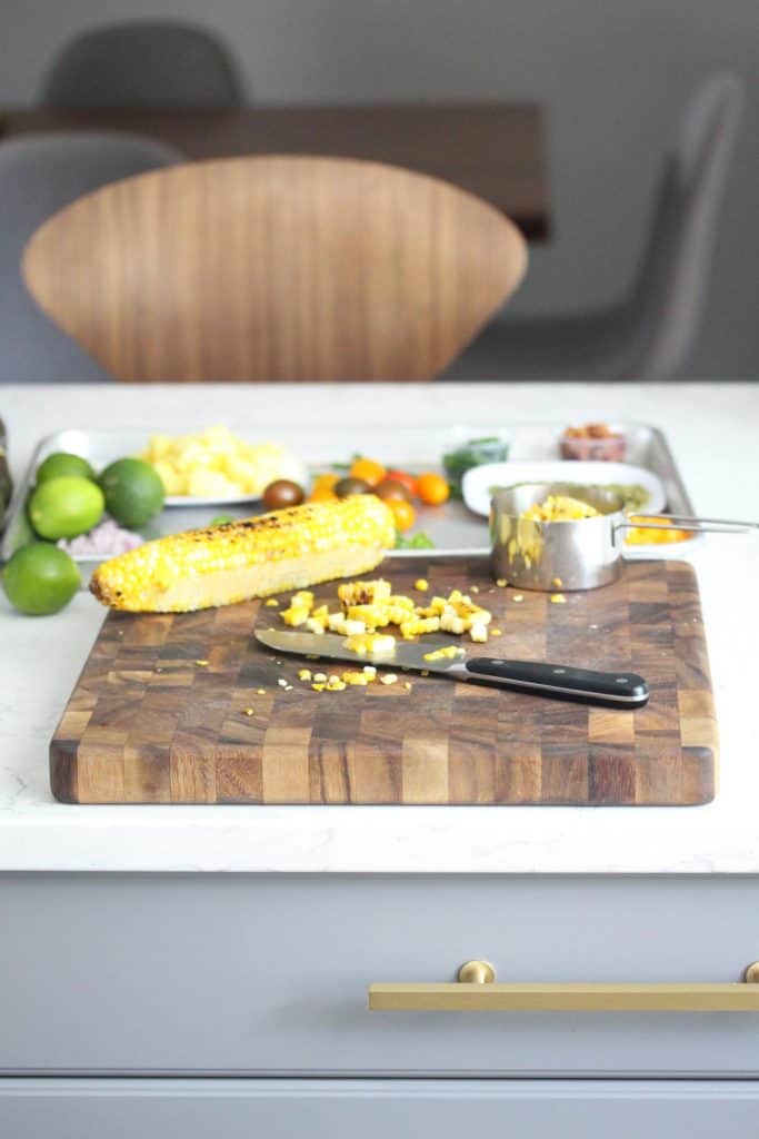 Corn and knife on brown cutting board on white counter.