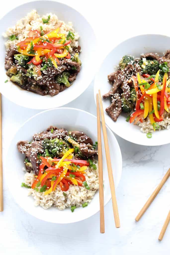 Beef and broccoli stir fry in three white bowls with chopsticks.