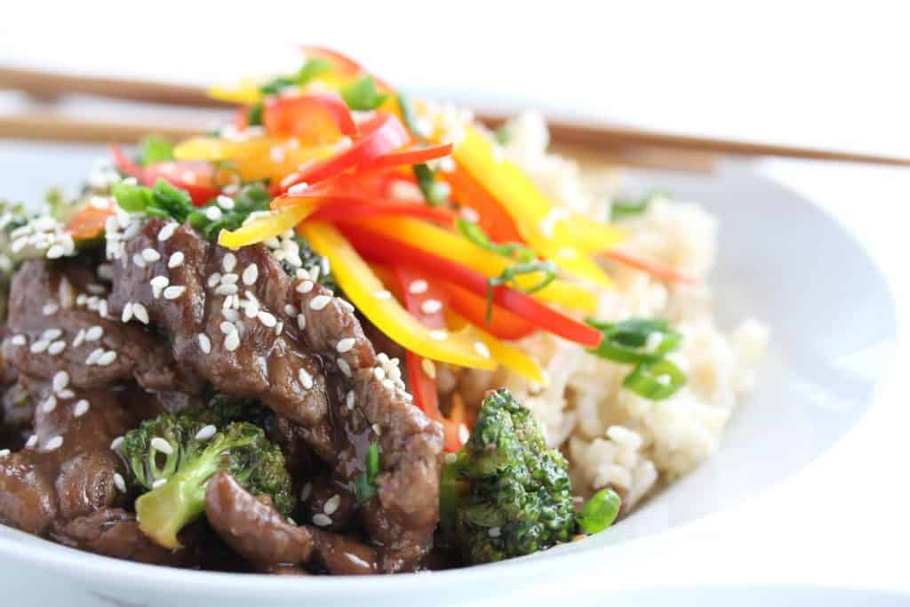 Beef and broccoli stir fry in white bowl with chopsticks.