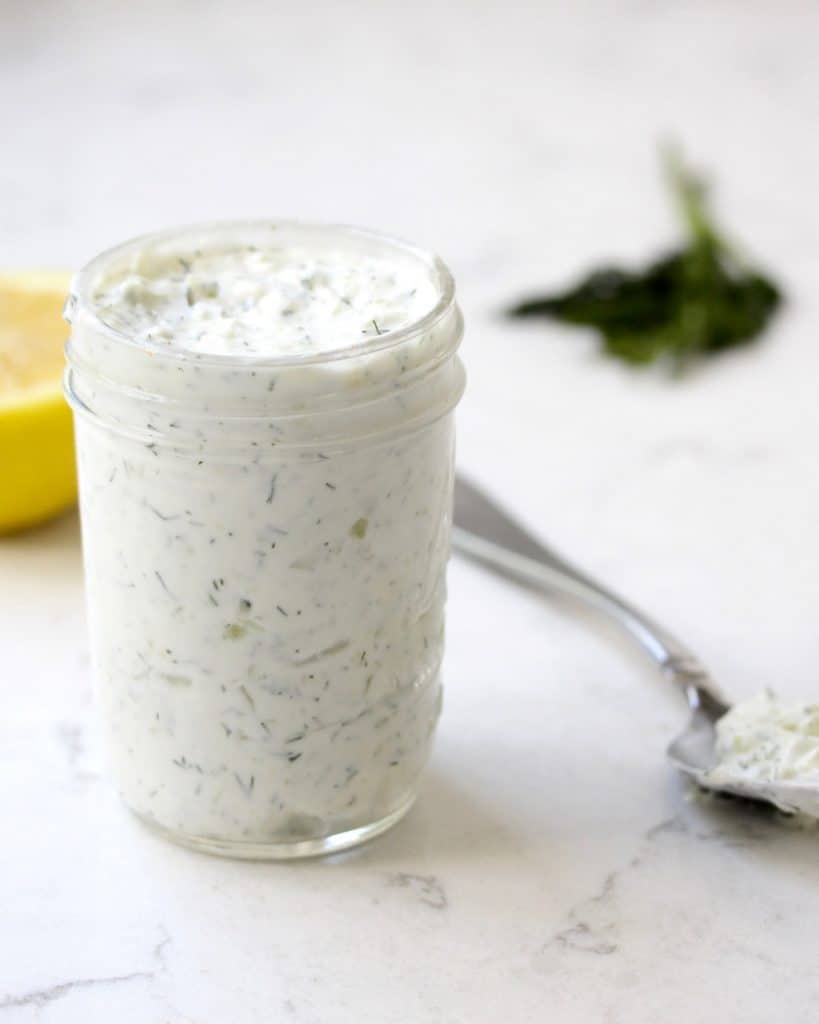 Tzatziki sauce in mason jar on marble surface.