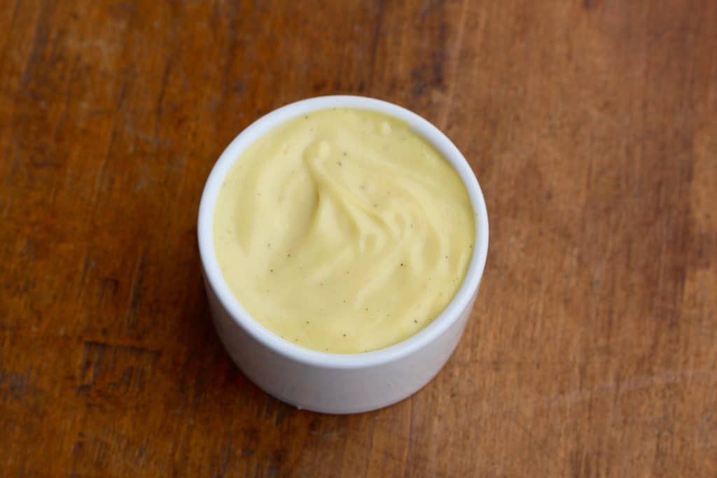 Hollandaise in white bowl on wood surface.