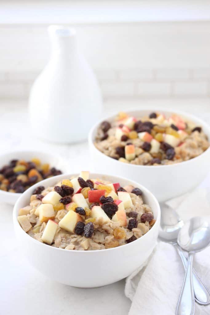 Apple raisin oatmeal in white bowl with two spoons.