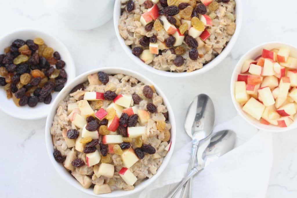 Apple raisin oatmeal in white bowl with two spoons.