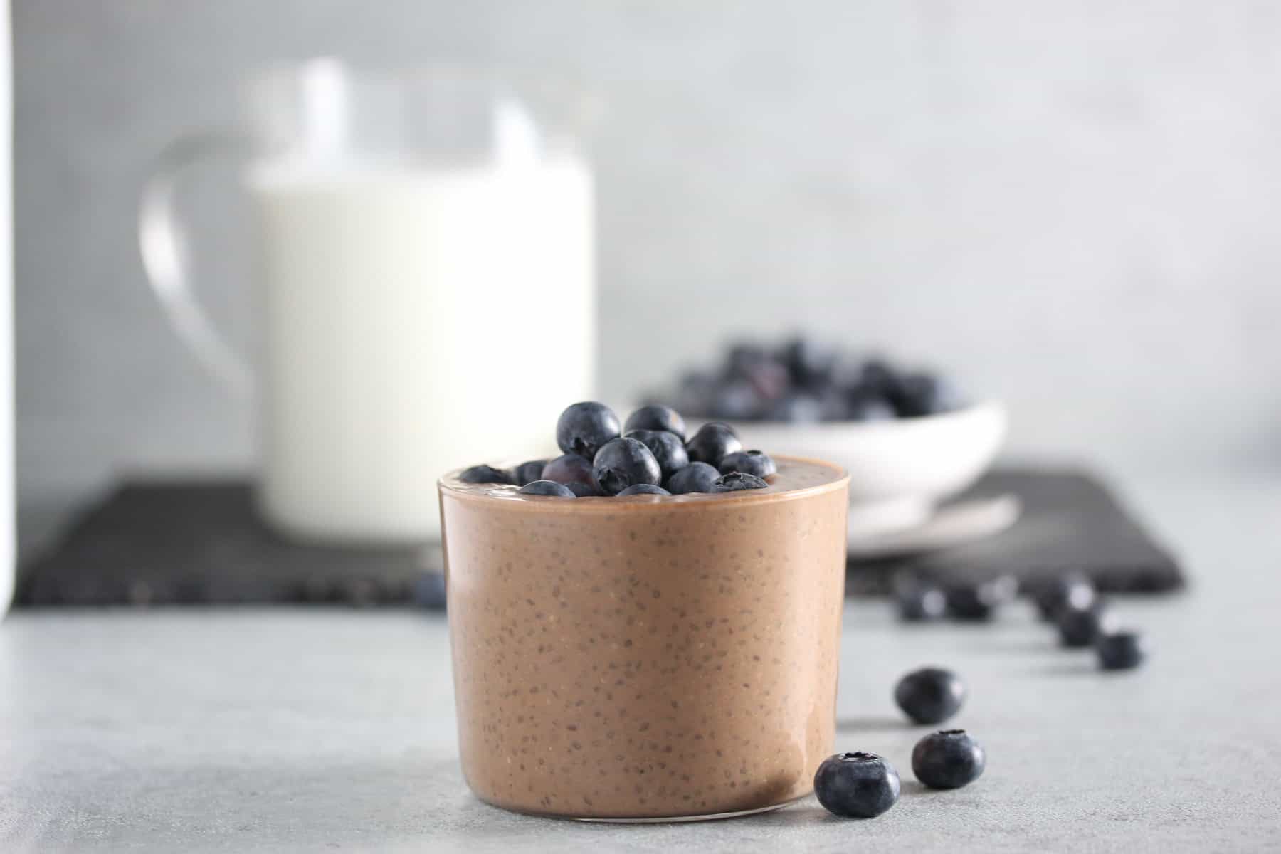 Chocolate pudding in glass on grey surface with blueberries.