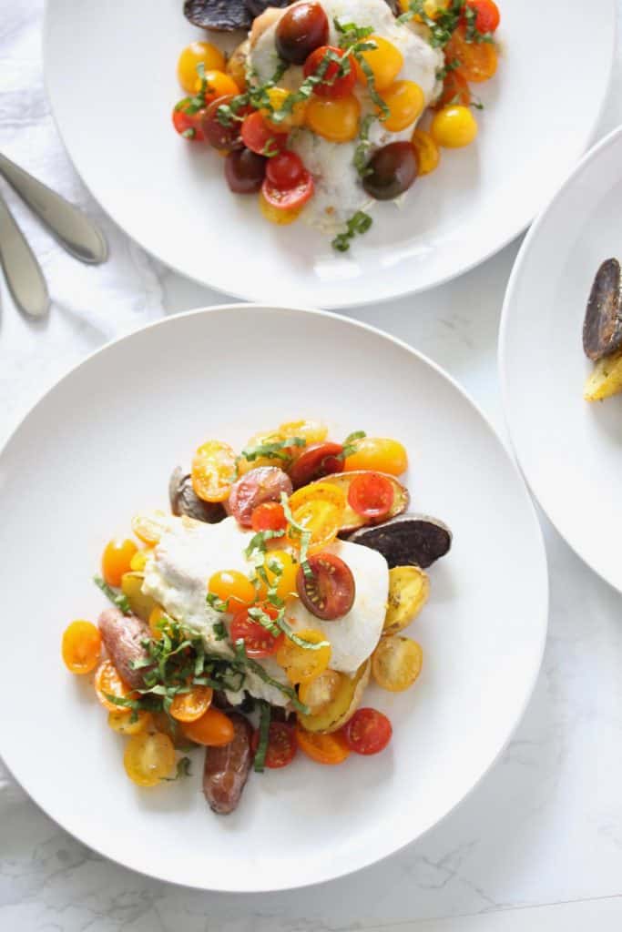 Chicken with tomatoes and potatoes on white plate.