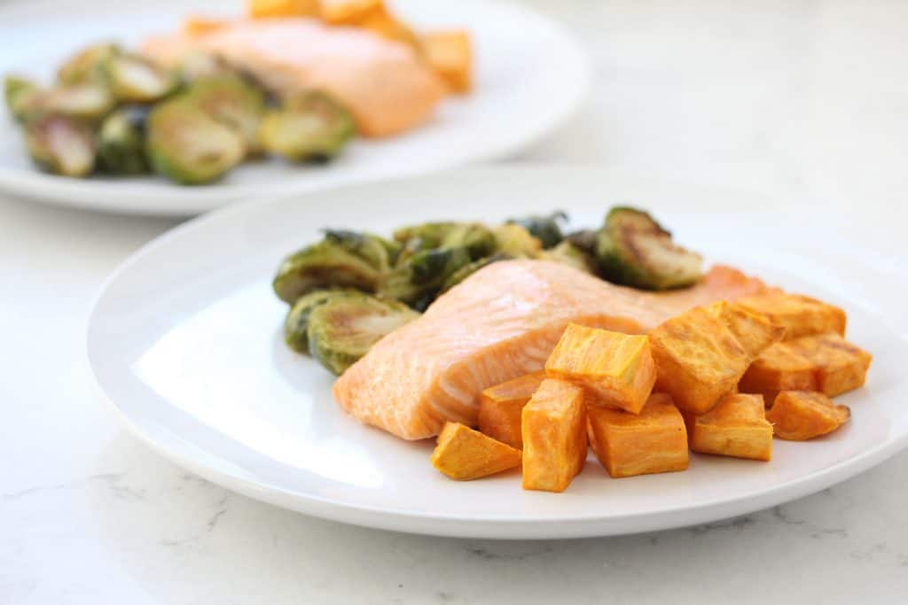 Salmon, sweet potatoes and Brussels sprouts on white plate.