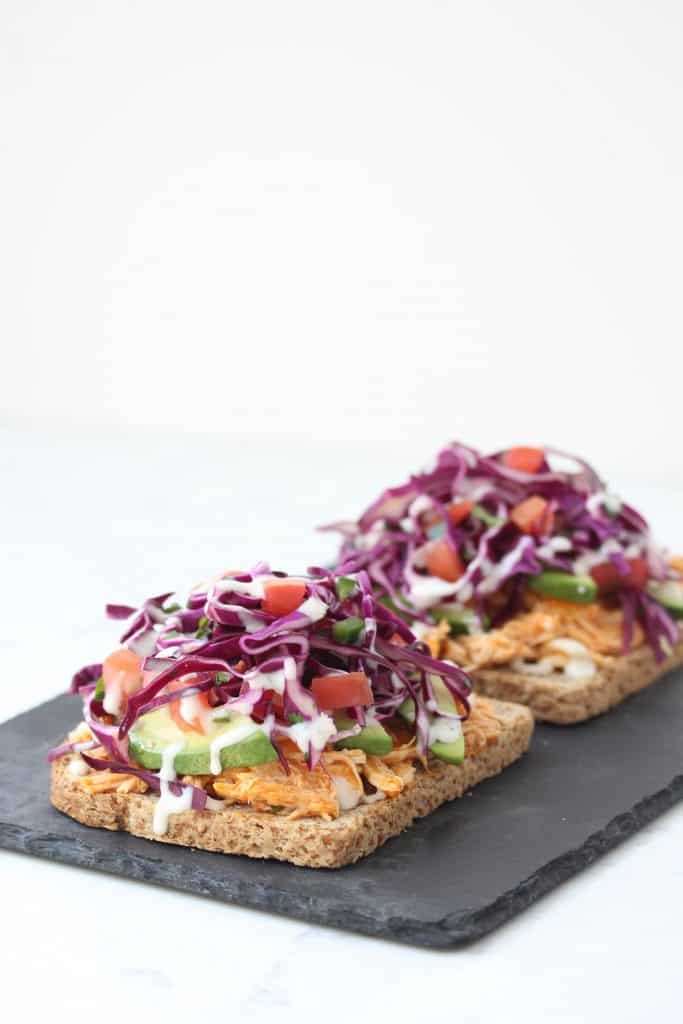 Open face buffalo chicken sandwich on grey stone cutting board.