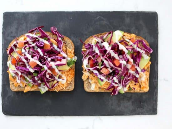 Open face buffalo chicken sandwich on grey stone cutting board.