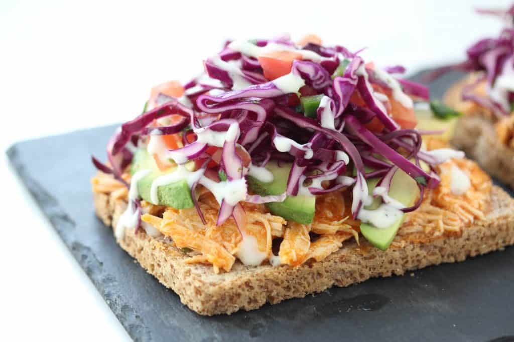 Open face buffalo chicken sandwich on grey stone cutting board.