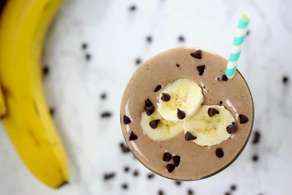 Chocolate smoothie with banana slices in clear glass on white surface.