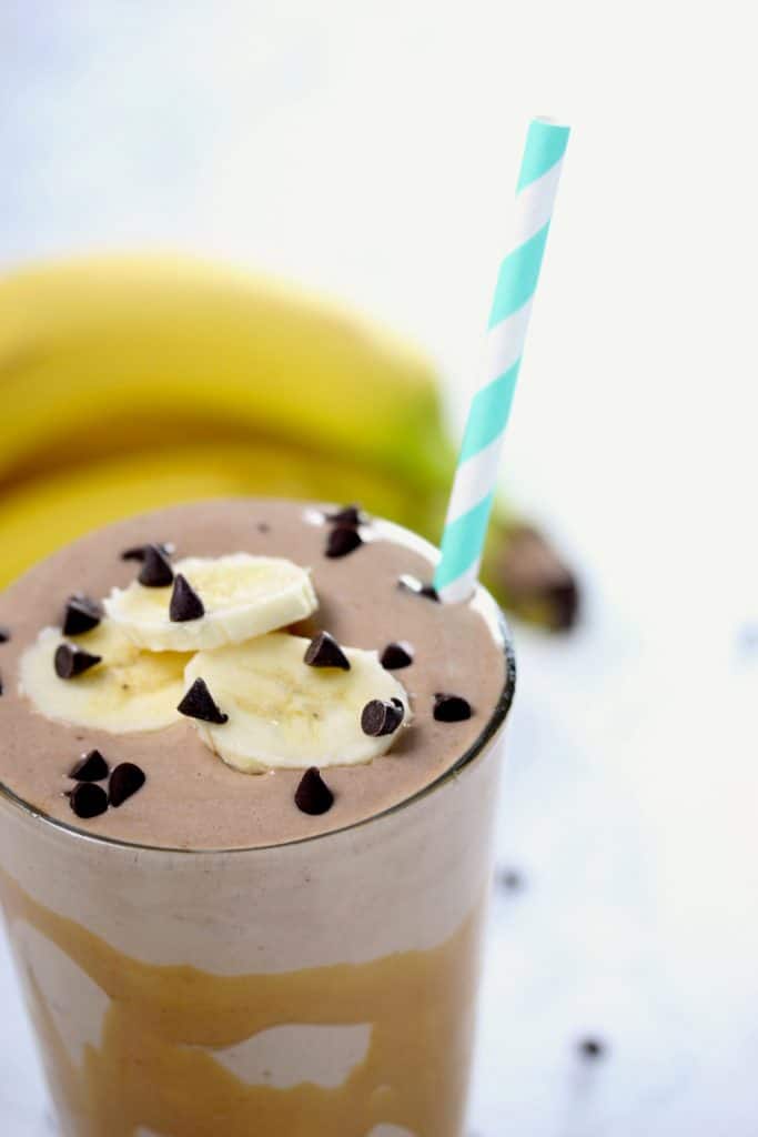 Chocolate smoothie with banana slices in clear glass on white surface.