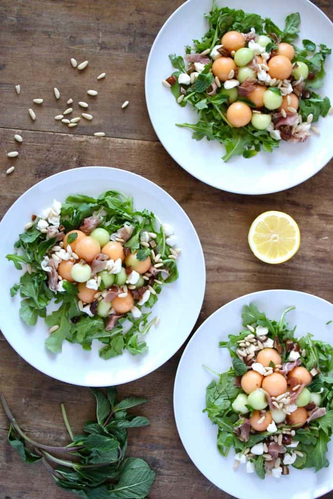 Salad on three white plates on wood surface.