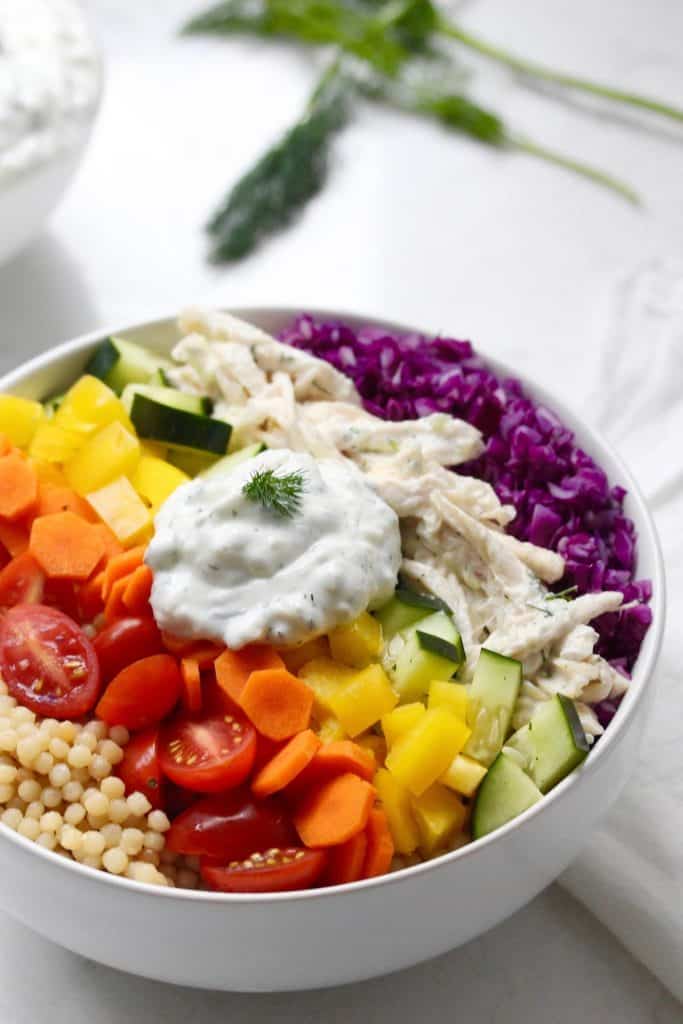 Fresh veggies, couscous and chicken in white bowl with Tzatziki sauce.