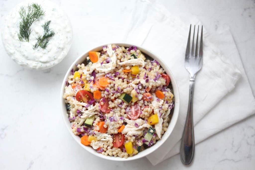 Fresh veggies, couscous and chicken in white bowl with Tzatziki sauce.