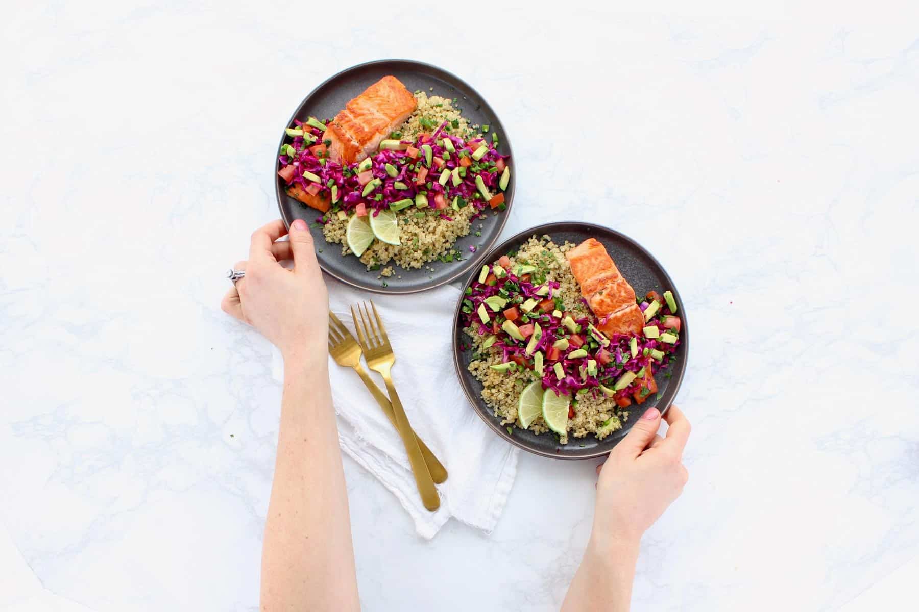 Salmon, quinoa and fresh vegetables on two grey plates.