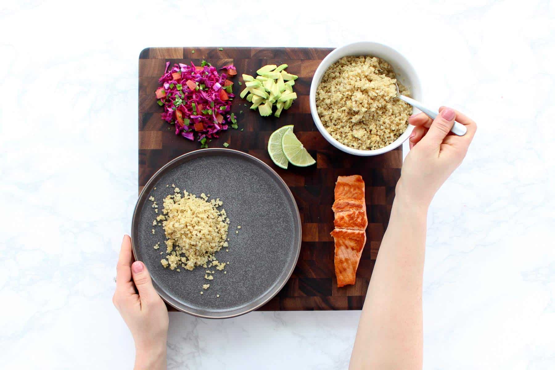 Two hands assembling salmon and rainbow quinoa recipe.