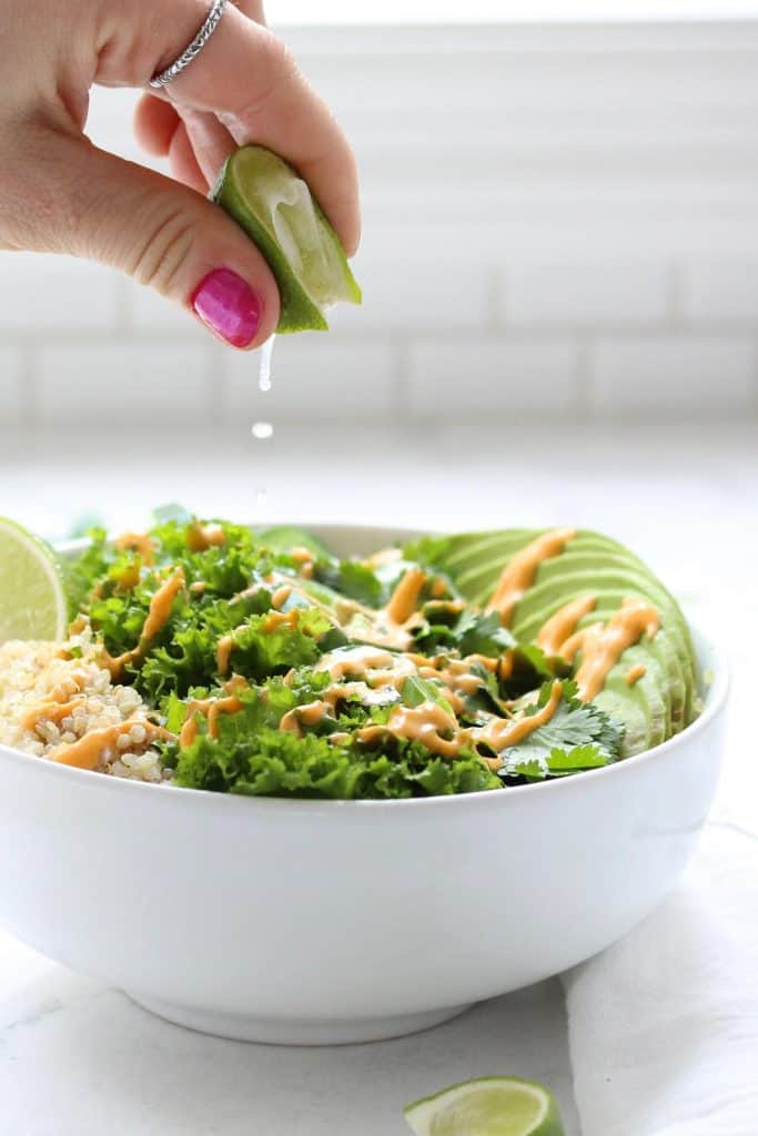 Hand squeezing lime over green grain bowl.