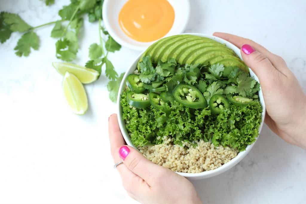 Two hands holding white bowl of greens and quinoa.