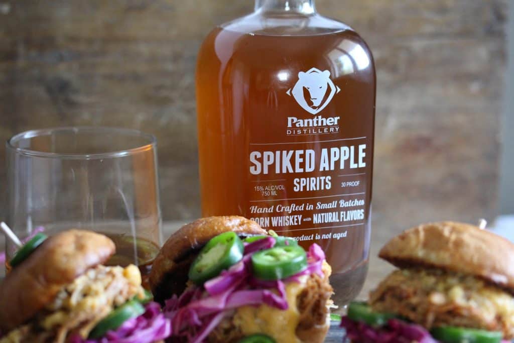 Pork sliders on grey cutting board with whiskey bottle.