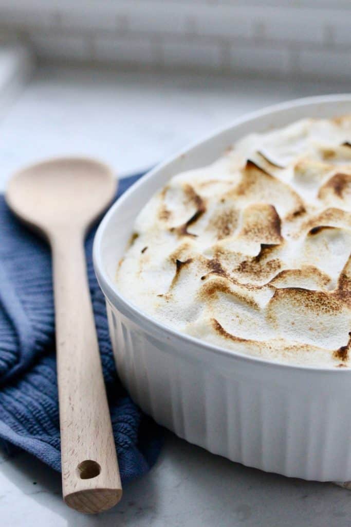 Sweet potato casserole in white dish with spoon and blue napkin.