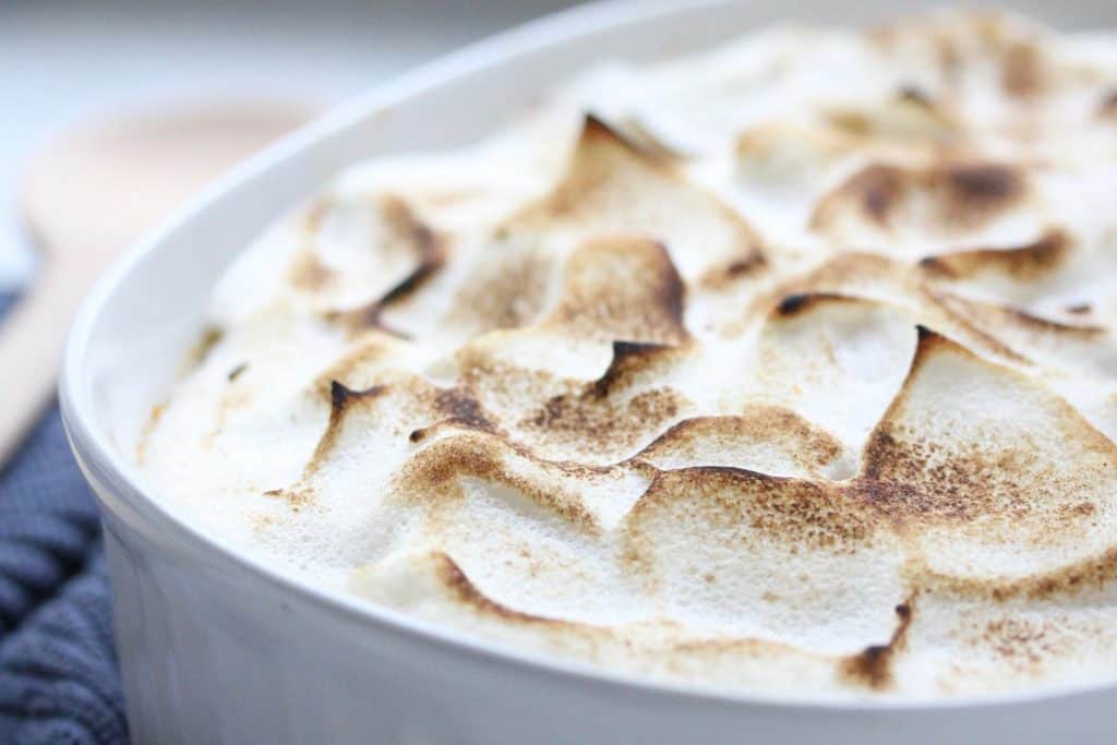 Sweet potato casserole in white dish with spoon and blue napkin.