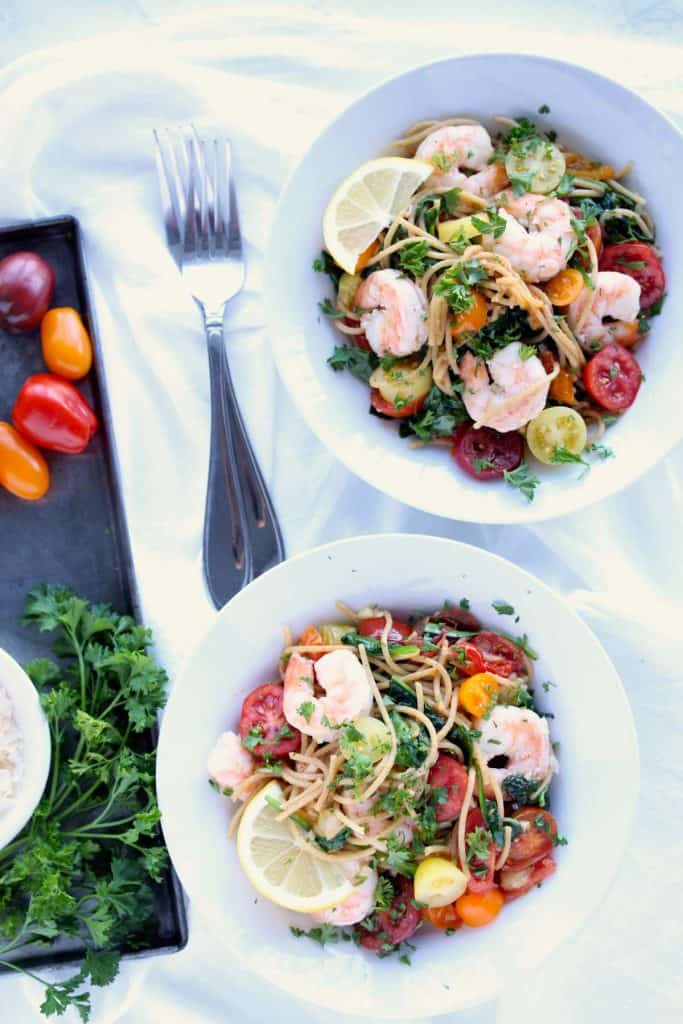 Two white bowls of shrimp pasta on white napkin.