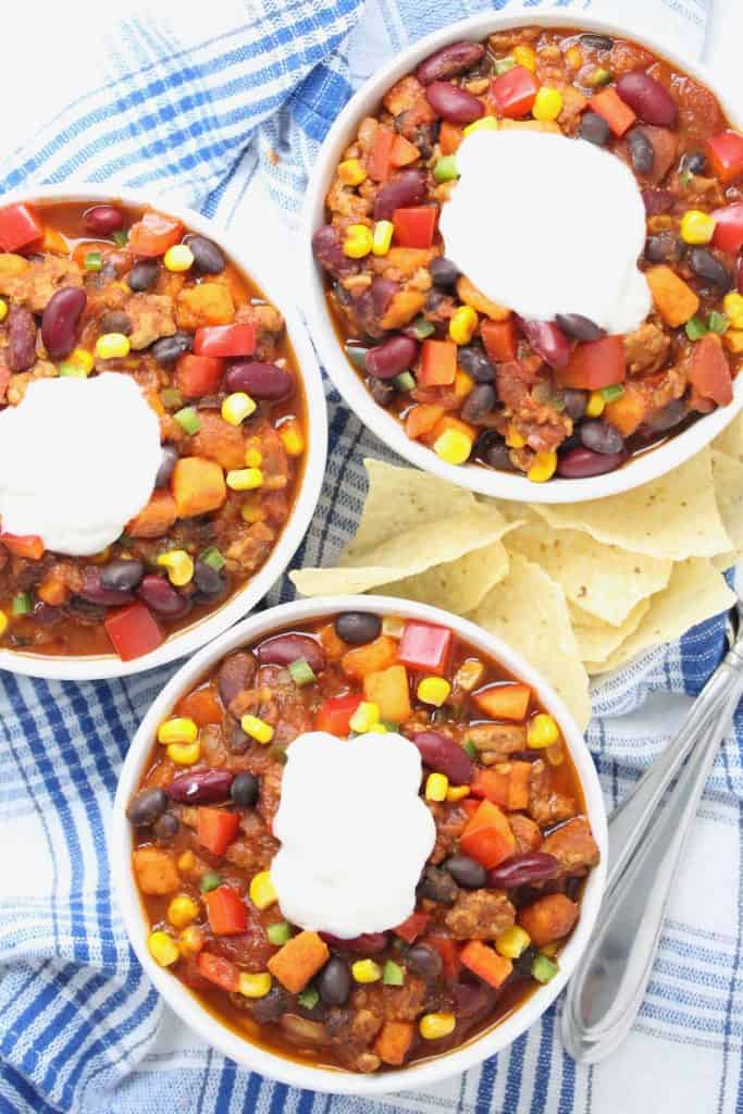 Chili in white bowls on blue plaid napkins.