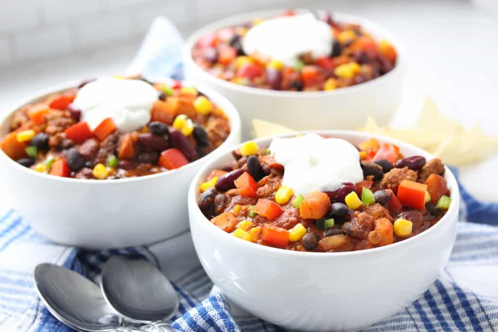 Chili in white bowls on blue plaid napkins.